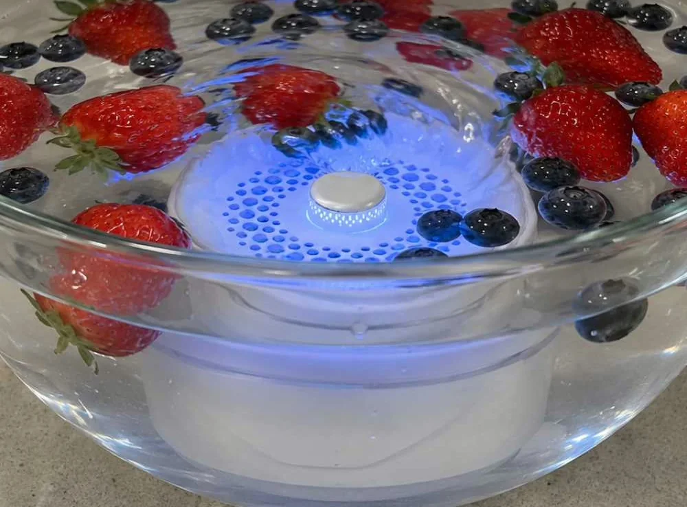 Saladier en verre rempli d'eau, de fraises et de myrtilles avec l'appareil PuriEasy allumé au fond